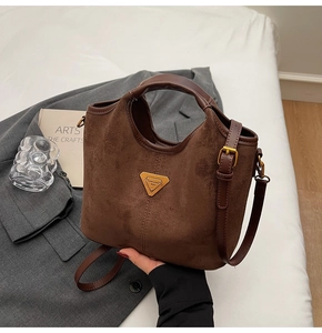 Détail de ce sac seau en daim marron mettant en valeur son logo triangulaire doré