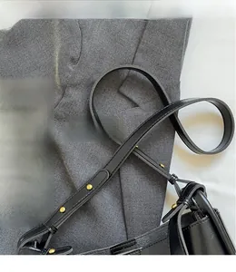 Detail showing adjustable black leather strap with gold metallic rivets on the bucket bag