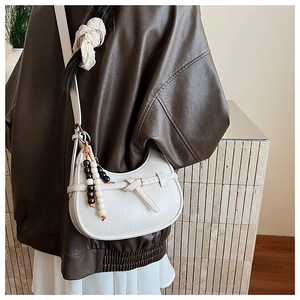 Close-up of off-white hobo bag with vintage beaded charm worn with a dark leather jacket
