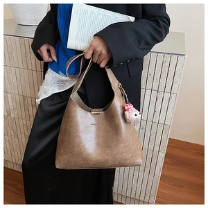 Detail of a brown leather Hobo bag with a plush pink fox charm and brand embossing