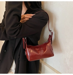 Detail of dark red crescent shoulder bag in glossy leather worn with a black blazer
