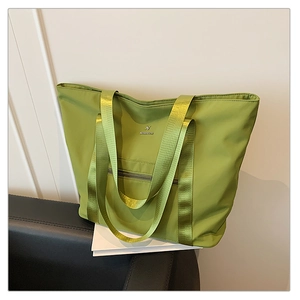 Détail du sac cabas en nylon vert montrant le tissu imperméable et le logo en métal