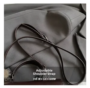 Detail of adjustable leather shoulder strap and plush ball charm on brown handbag
