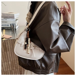 Close-up of cream half-moon crossbody bag with vintage wooden bead tassel detail
