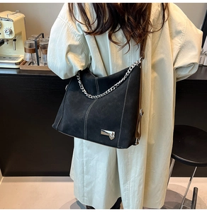 Detailed close-up of a black suede crossbody bag with silver chain and white stitching