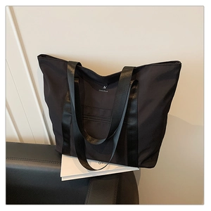 Détail du sac cabas en nylon noir étanche montrant le logo métallique et les anses larges