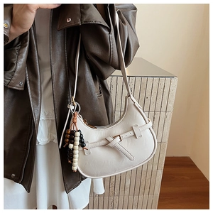 Close-up of minimalist cream half-moon crossbody bag with decorative bead charms