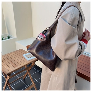 Detail of vintage brown leather tote bag featuring a cute plush bear charm accessory