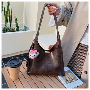 Detailed view of brown vintage PU leather hobo bag with plush charm on a wooden table