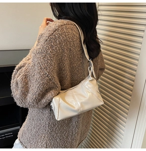 Detail view of cream-white leather shoulder bag with elegant pleated texture on a model
