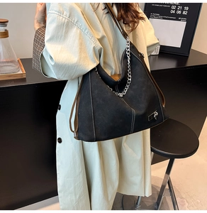 Street style view of a large black suede tote bag with white stitching and silver chains