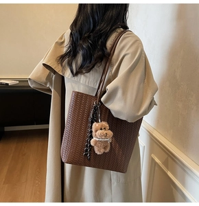 Detail of dark brown woven tote bag featuring a plush bear charm and striped ribbon accent