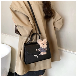 Detail of black glossy leather handbag with silver twist lock and teddy bear pendant