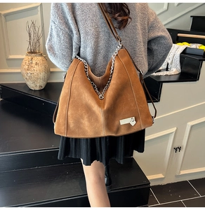 Close-up of brown suede hobo bag featuring silver chain trim and a heart charm pendant