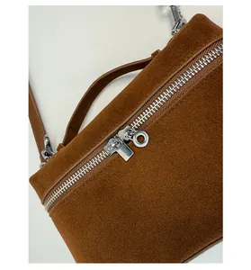 Detail einer braunen Wildleder-Box-Tasche mit silbernem Reißverschluss und Ringgriff