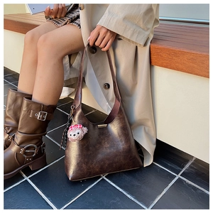 Detail of vintage brown leather shoulder bucket bag with stylish plush pendant accessory