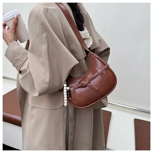 Detail of dark brown leather crescent bag with decorative strap and wooden bead charm