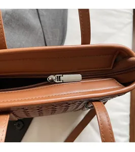 Detailed close-up of smooth silver zipper closure on brown woven leather tote bag
