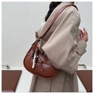 Detail of a brown crescent shoulder bag with leather strap and decorative bead charm