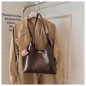 Detail of dark brown vintage leather hobo bag with a plush doll charm on a coat rack