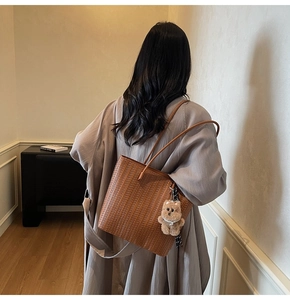 Rear view of a model wearing the brown woven tote bag with a cute bear charm accessory