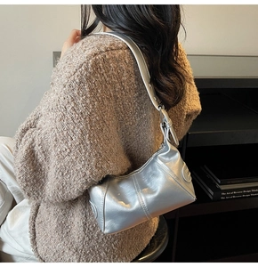 Silver metallic shoulder bag with pleated texture worn by model in brown knit sweater
