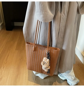 Close-up of brown woven tote bag featuring a plush dog charm and checkered scarf detail
