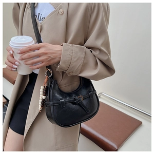 Detail of black crescent shoulder bag featuring gold buckle and wooden bead charm accessory