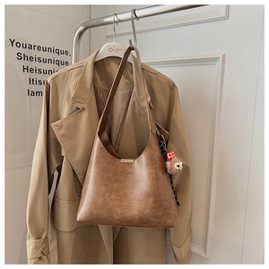 Brown vintage PU leather bucket bag with cute plush charm on a coat rack display