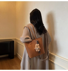 Detailed view of brown woven tote bag with cute bear charm worn by a model