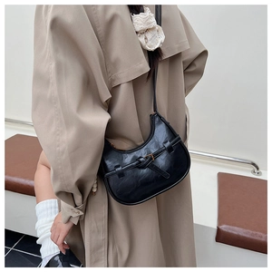 Detail view of black crescent moon bag with metal buckle on beige trench coat