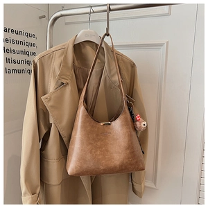 Detailed view of brown retro textured shoulder bag with a plush bear charm on a coat rack