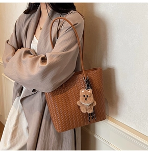 Close-up of brown woven tote bag with cute plush bear pendant and thin shoulder straps