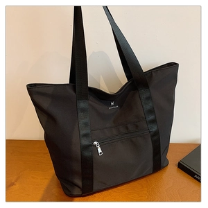 Détail du grand sac cabas noir en tissu Oxford avec poche zippée sur une surface en bois