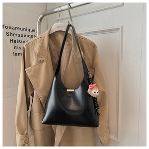 Detail of black leather underarm bag with gold buckle and a pink plush fox pendant