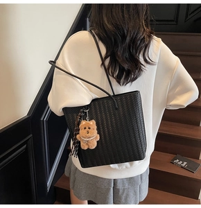 Detail of black woven tote bag with cute bear charm worn over the shoulder