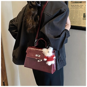 Detail view of dark red leather handbag with silver lock and bear charm accessory
