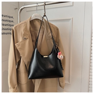 Detail of a black faux leather bucket bag with a pink sheep charm on a beige trench coat