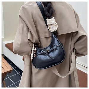 Detail of black crescent bag with belt buckle and decorative wooden beads on beige coat
