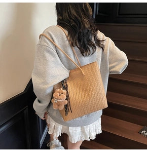 Detail of a brown woven tote bag featuring a V-shaped pattern and a cute plush bear charm