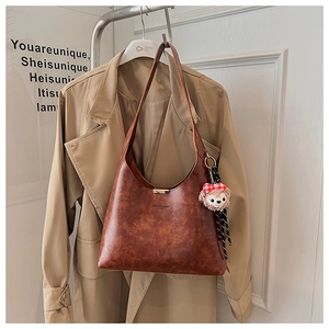 Detail of vintage brown tote bag with metal buckle and plush bear charm on a beige coat