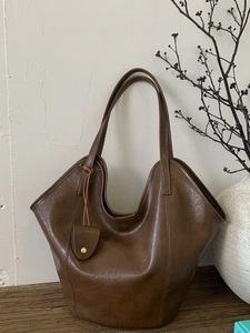 Retro dark brown leather tote bag with curved top handle in a minimalist interior setting