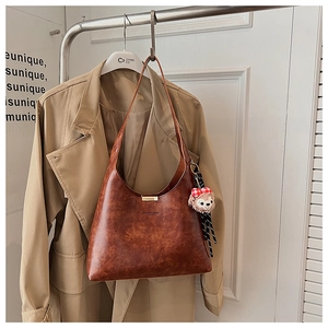 Vintage brown leather shoulder bag with gold clasp and plush charm on a trench coat