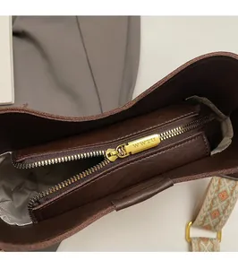 Detailed macro of smooth gold zipper and ethnic woven strap on brown leather bucket bag
