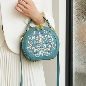 Detailed close-up of intricate ethnic floral embroidery on a round teal leather handbag