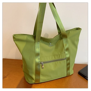 Gros plan du cabas en tissu Oxford vert avec poche zippée et logo métallique de marque