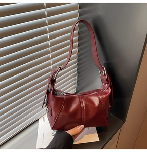 Detail of burgundy ruched shoulder bag with glossy PU finish and adjustable silver buckle