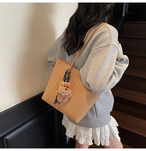 Detail of light brown woven tote bag with plush bear charm and striped ribbon accent