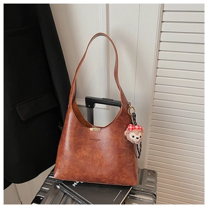 Detail of caramel leather tote bag with metallic magnetic buckle and plush bear pendant