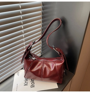 Macro view of burgundy glossy leather underarm bag featuring a silver star zipper pull